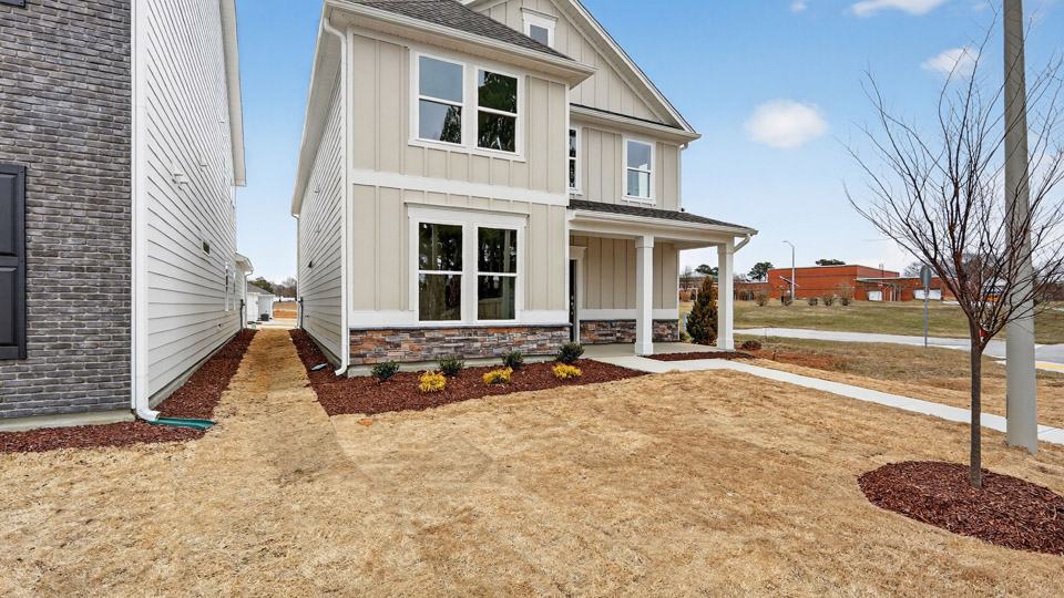 Two story home with tan colored siding with a two car garage in the back of the house