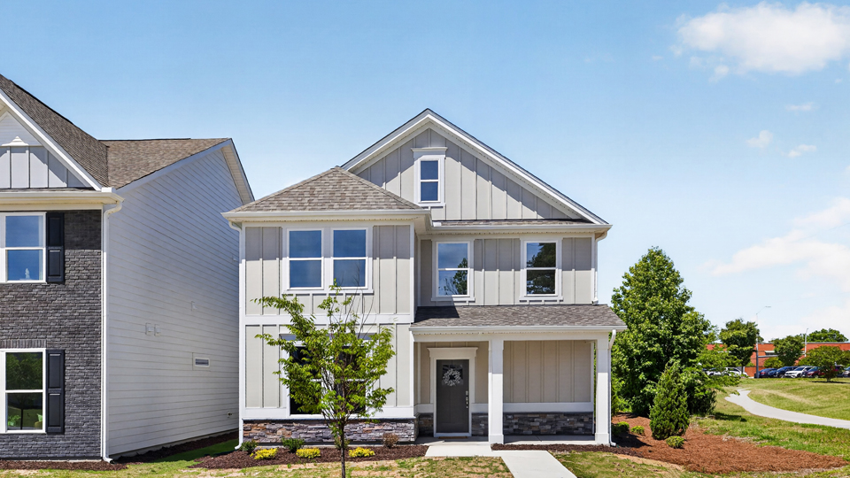 Two story home with tan colored siding with a two car garage in the back of the house