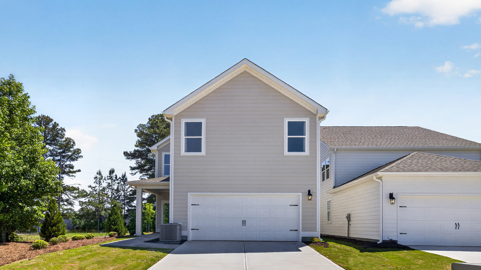 Two story home with tan colored siding with a two car garage in the back of the house