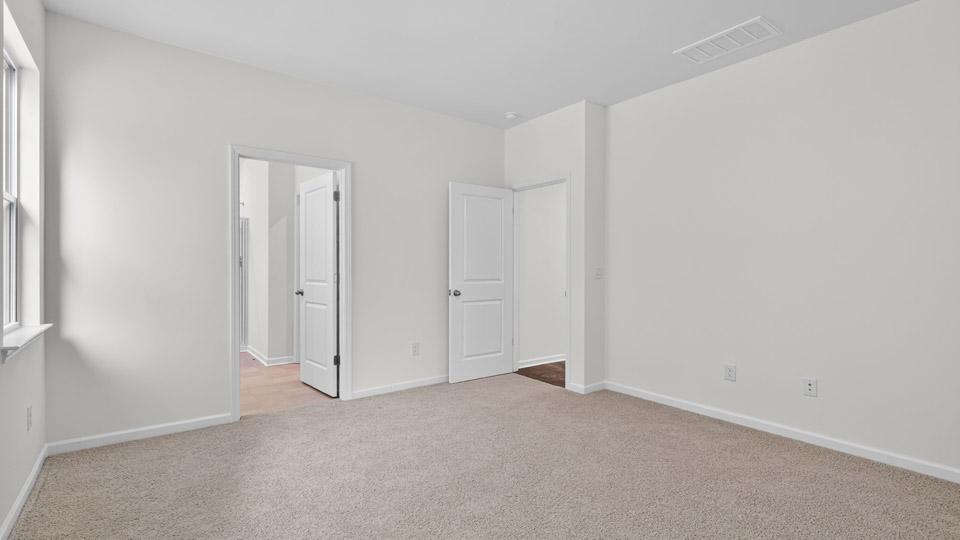 Primary bedroom with carpet floors and windows with access to the primary bathroom