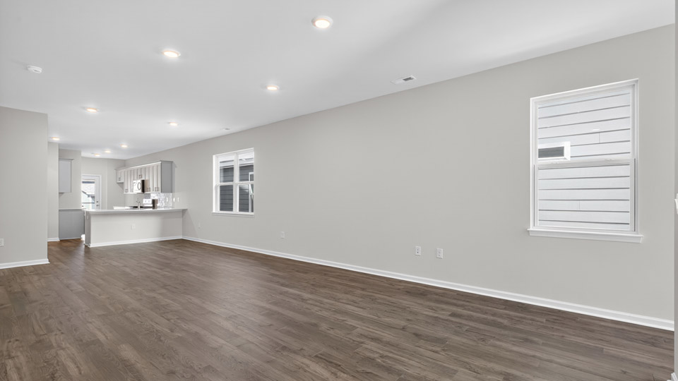 Open-concept living room with hardwood floors with windows leading to kitchen