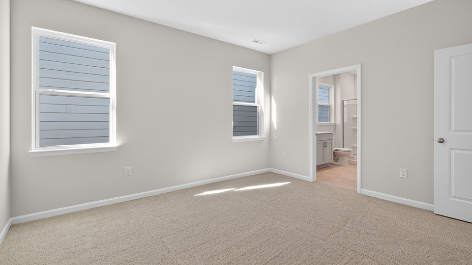 Primary bedroom with carpet floors and windows with access to the primary bathroom