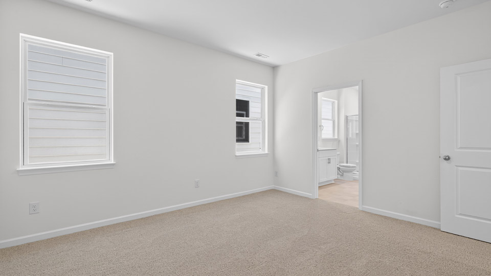 Primary bedroom with carpet floors and windows with access to the primary bathroom