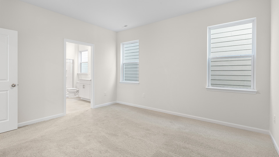 primary bedroom with two windows and carpeting, attached bath