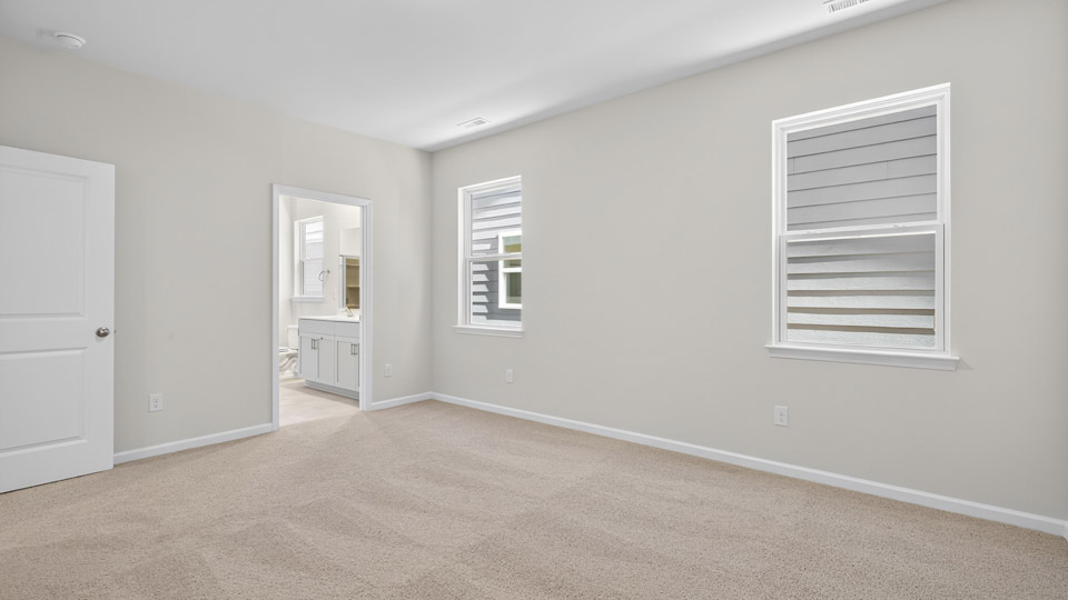 Primary bedroom with carpet floors and windows with access to the primary bathroom