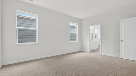 primary bedroom with two windows and carpeting, attached bath