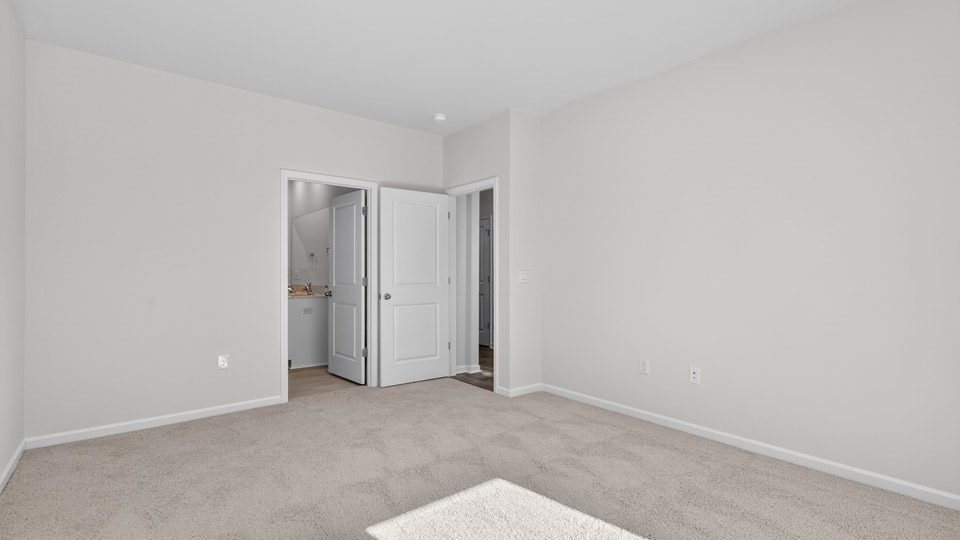 Primary bedroom with carpet floors and windows with access to the primary bathroom