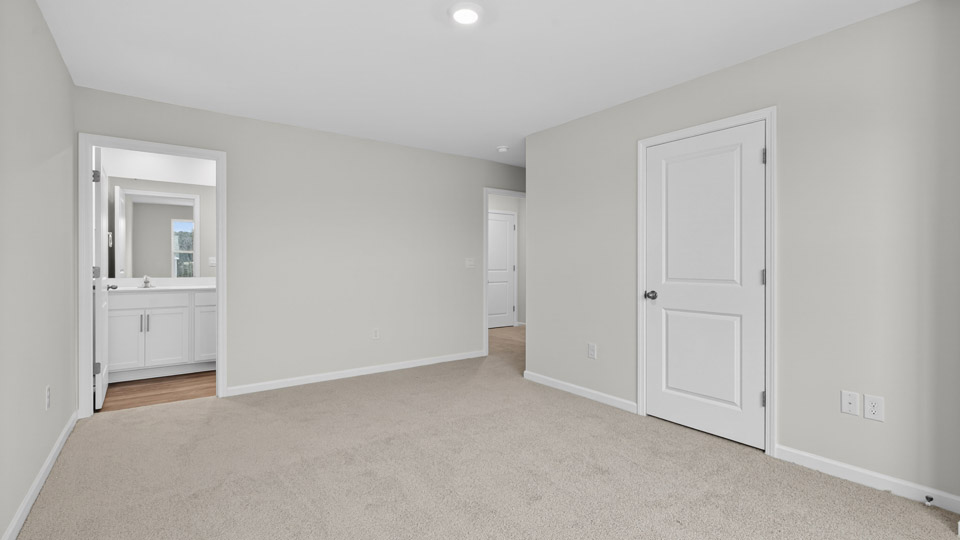 Primary bedroom with carpet floors and windows with access to the primary bathroom