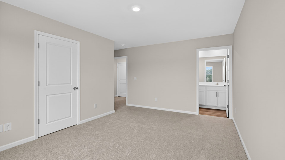 Primary bedroom with carpet floors and windows with access to the primary bathroom