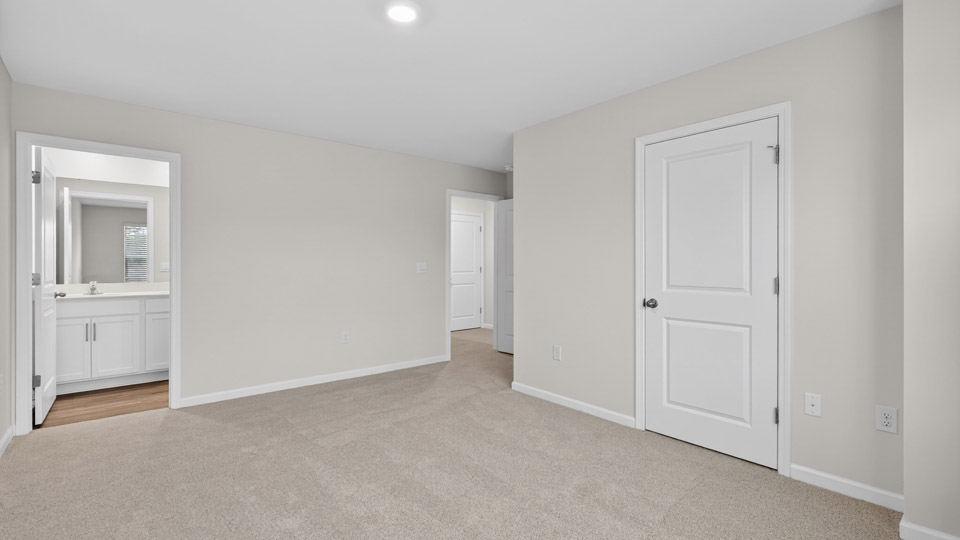 Primary bedroom with carpet floors and windows with access to the primary bathroom
