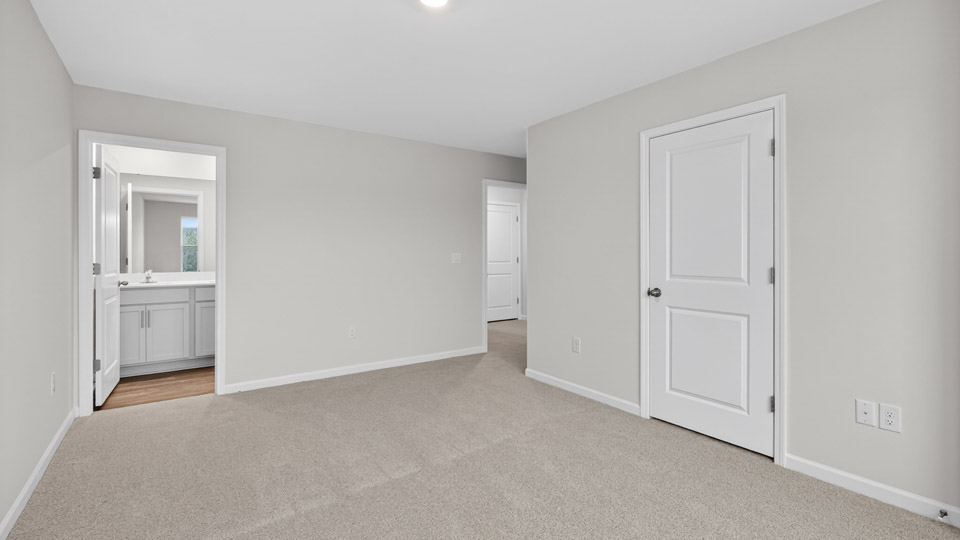 Primary bedroom with carpet floors and windows with access to the primary bathroom