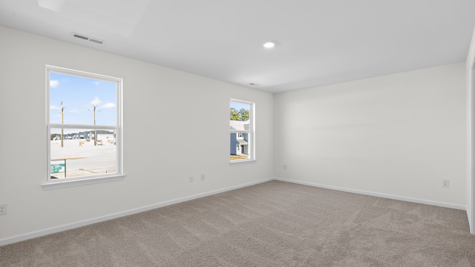 Primary bedroom with carpet floors and windows with access to the primary bathroom