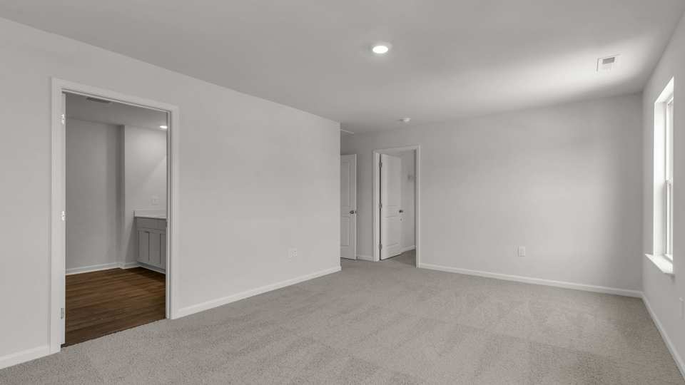 primary bedroom with two windows and carpeting, attached bath