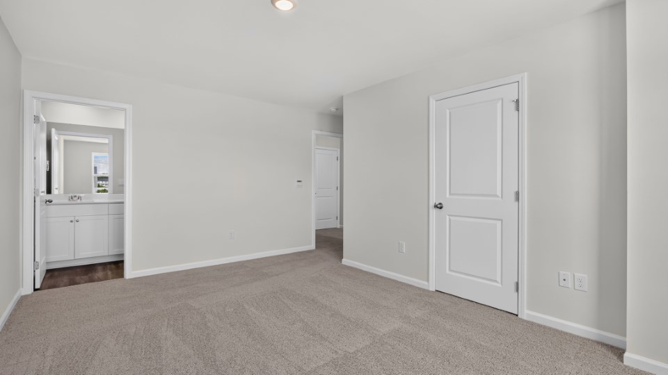 primary bedroom with two windows and carpeting, attached bath