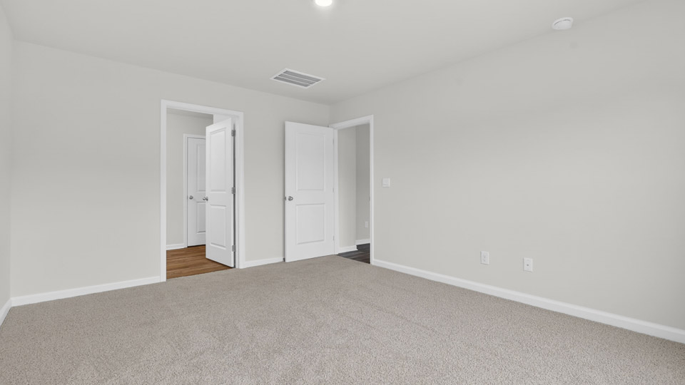Primary bedroom with carpet floors and windows with access to the primary bathroom