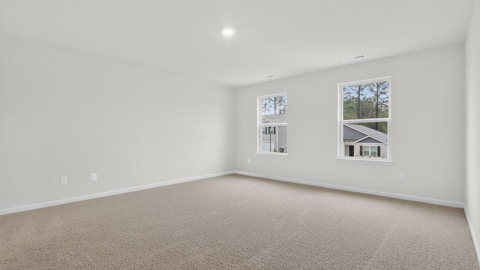 Primary bedroom with carpet floors and windows with access to the primary bathroom