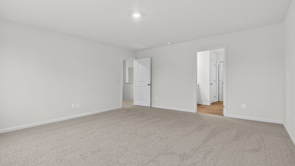 Primary bedroom with carpet floors and windows with access to the primary bathroom