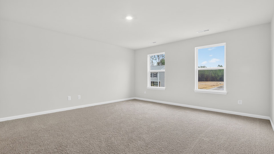 Primary bedroom with carpet floors and windows with access to the primary bathroom