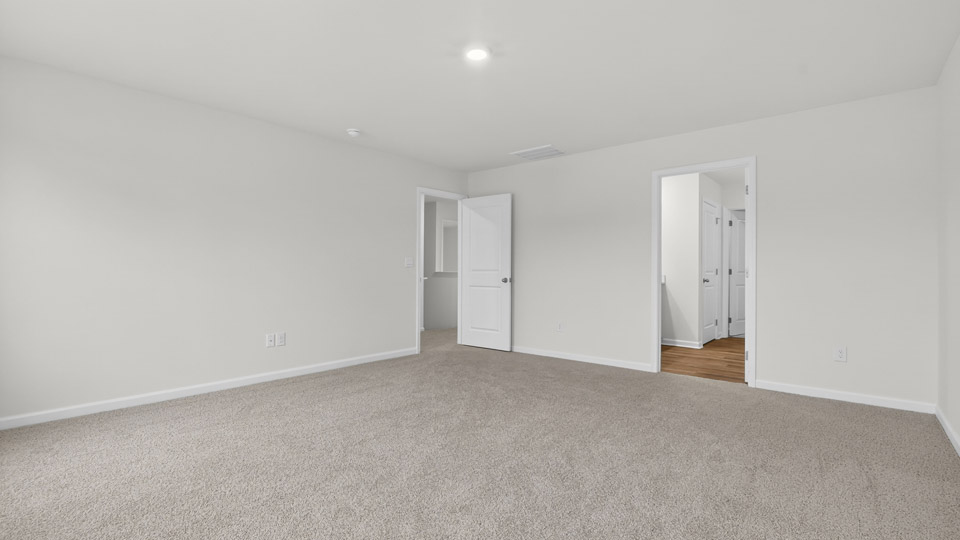 Primary bedroom with carpet floors and windows with access to the primary bathroom
