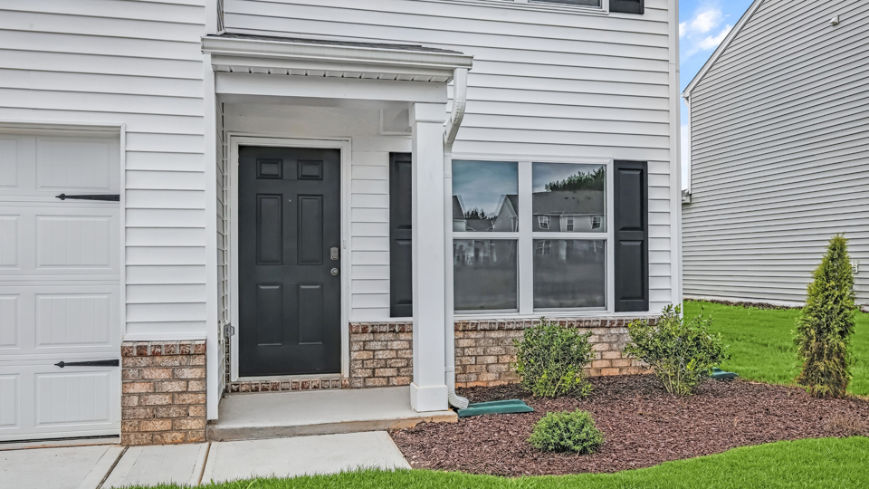 front door of belhaven floorplan with white siding, black shutters, and brick accent