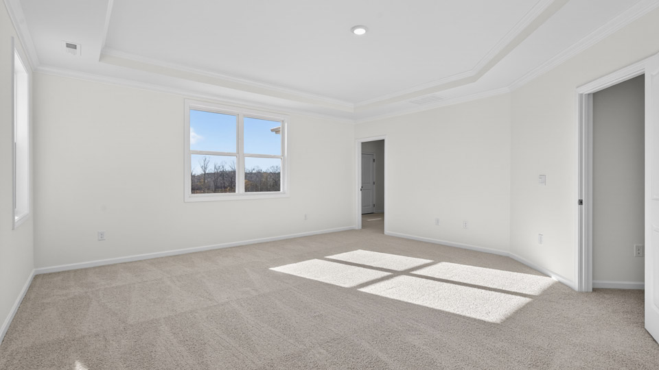Primary bedroom with carpet floors and windows with access to the primary bathroom