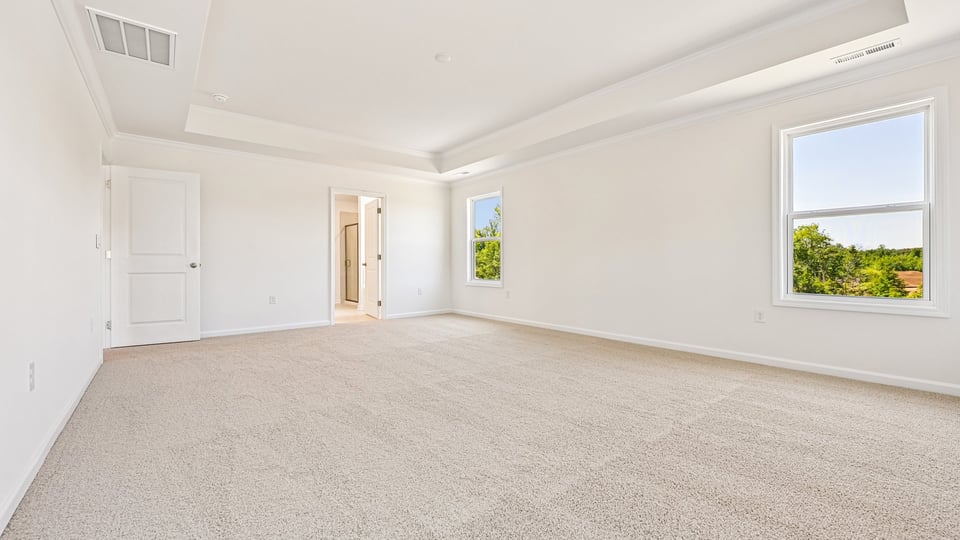 primary bedroom with two windows and carpeting, attached bath