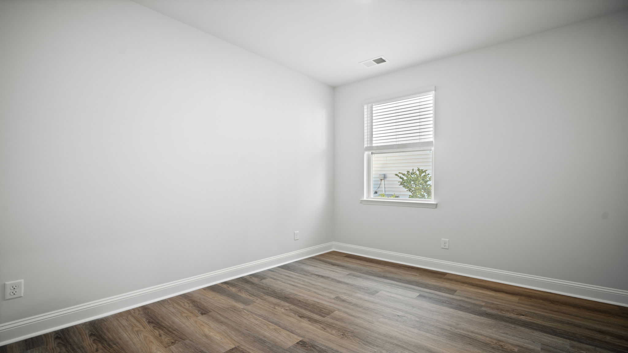 Secondary bedroom with large window, neutral walls, wood-look flooring, and flexible space for guests or a home office.