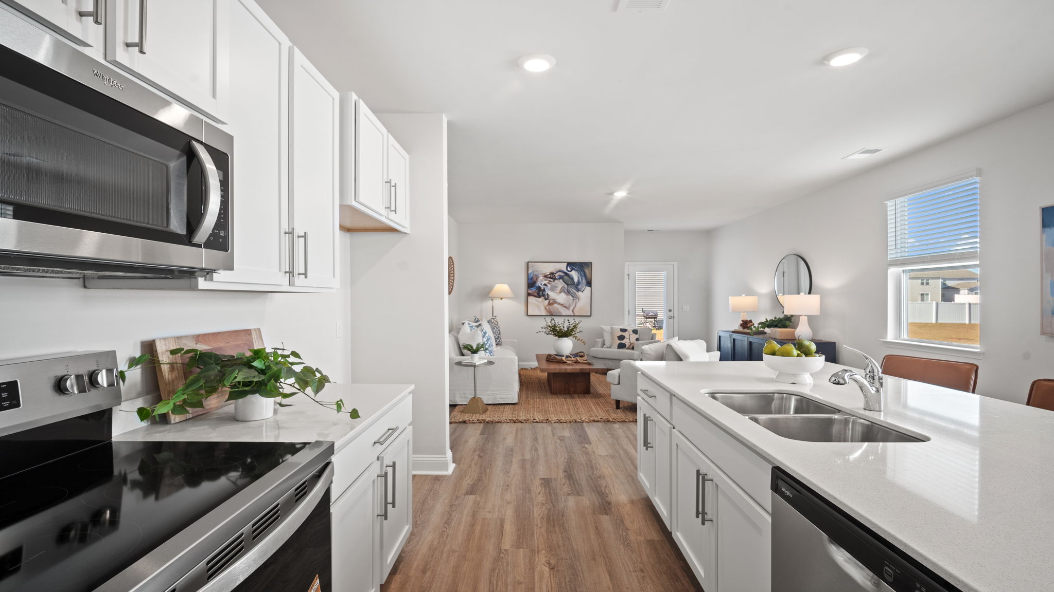 Modern kitchen with quartz countertops, stainless steel appliances, oversized island with sink, and view into the spacious living room.