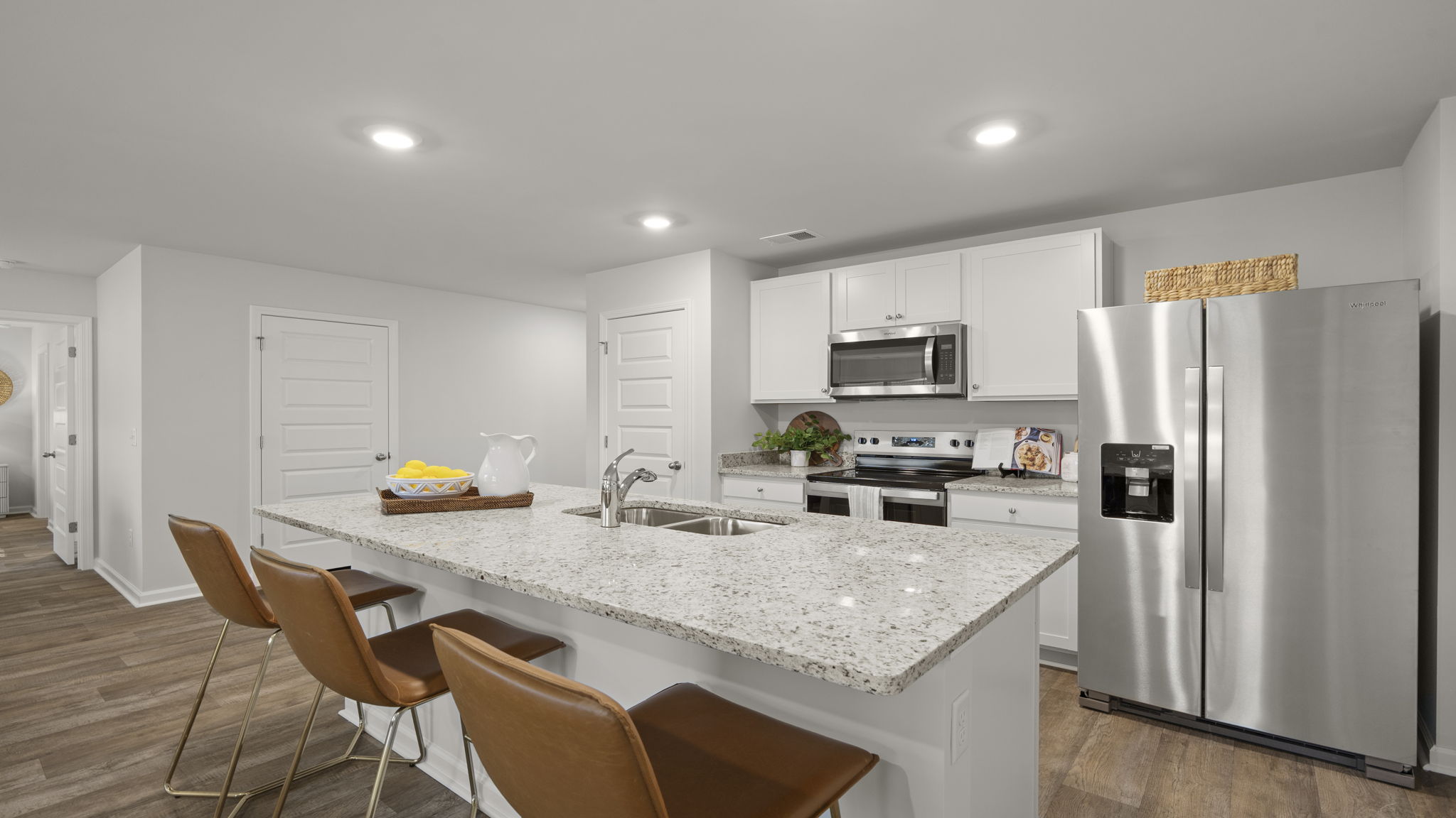 Open-concept kitchen featuring oversized granite island, stainless steel appliances, white cabinetry, recessed lighting, and breakfast seating.