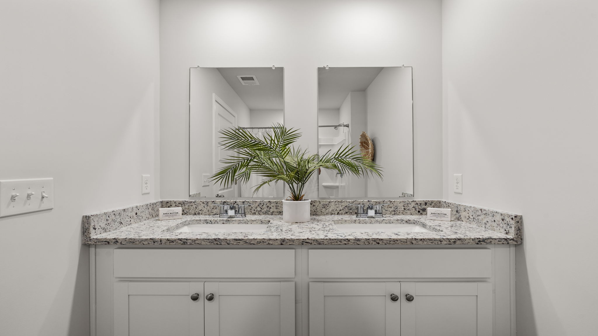 Double vanity in primary bath with granite countertops, ample storage, and updated lighting.
