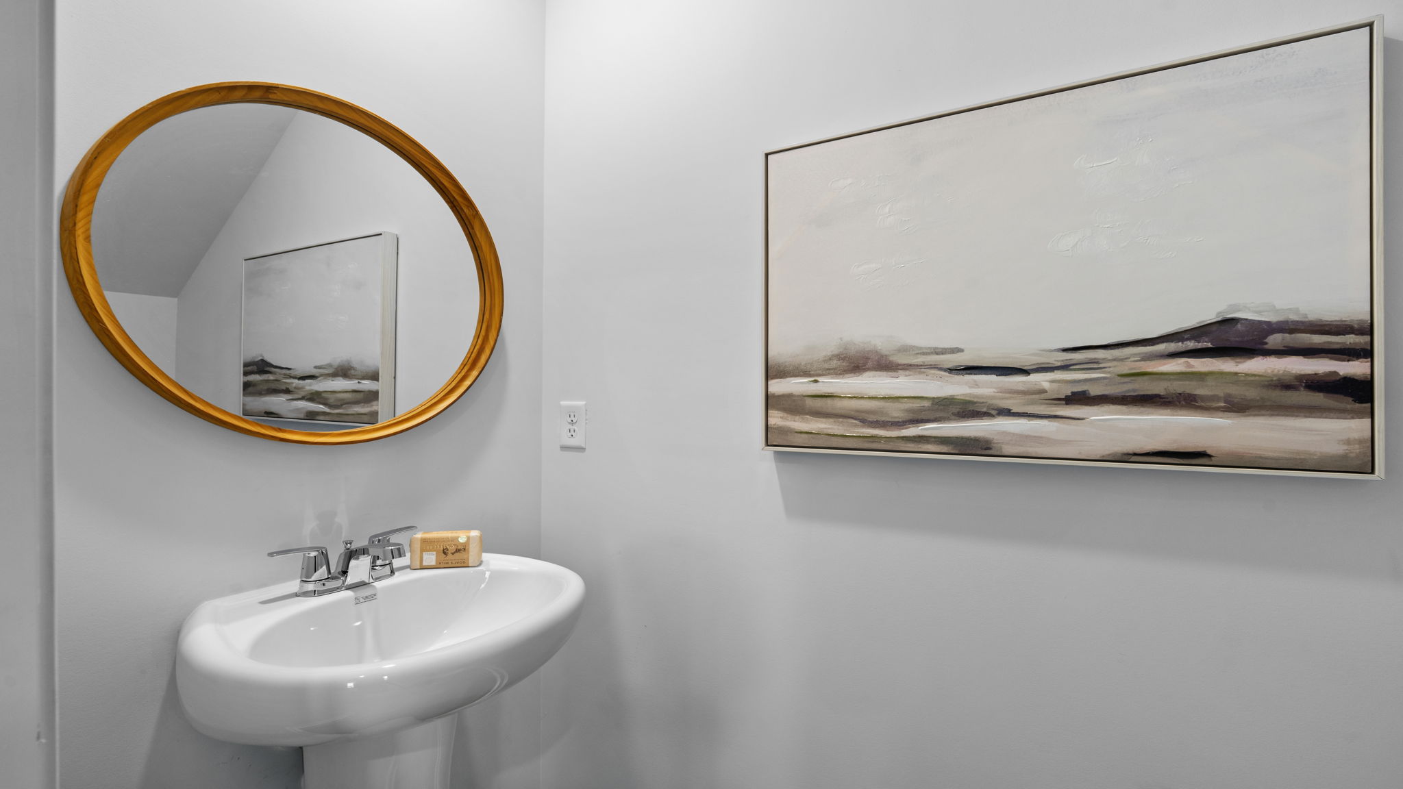 Half bathroom with pedestal sink and round mirror