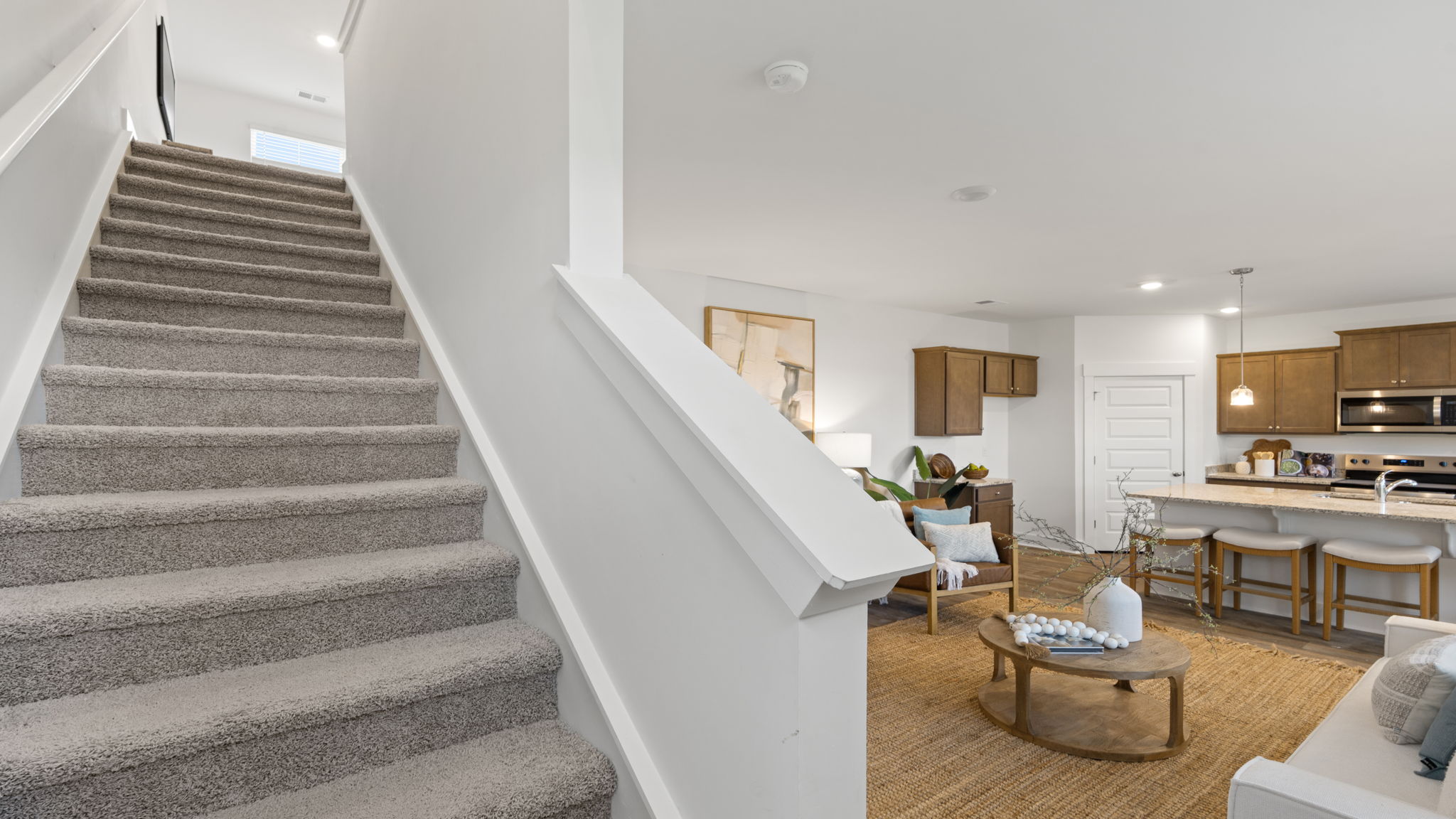 Staircase and open living area featuring light flooring and neutral interior finishes.