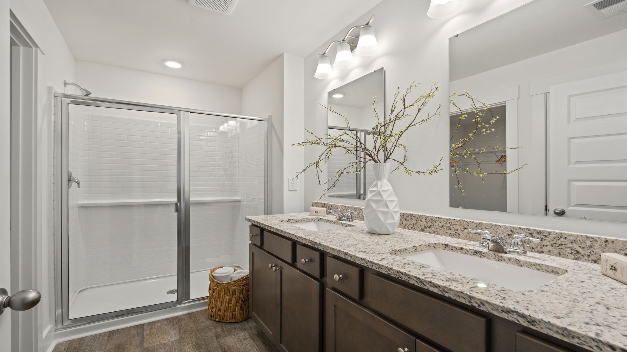 Bathroom with dual-sink vanity, large mirror, dark cabinetry, and glass-enclosed shower.