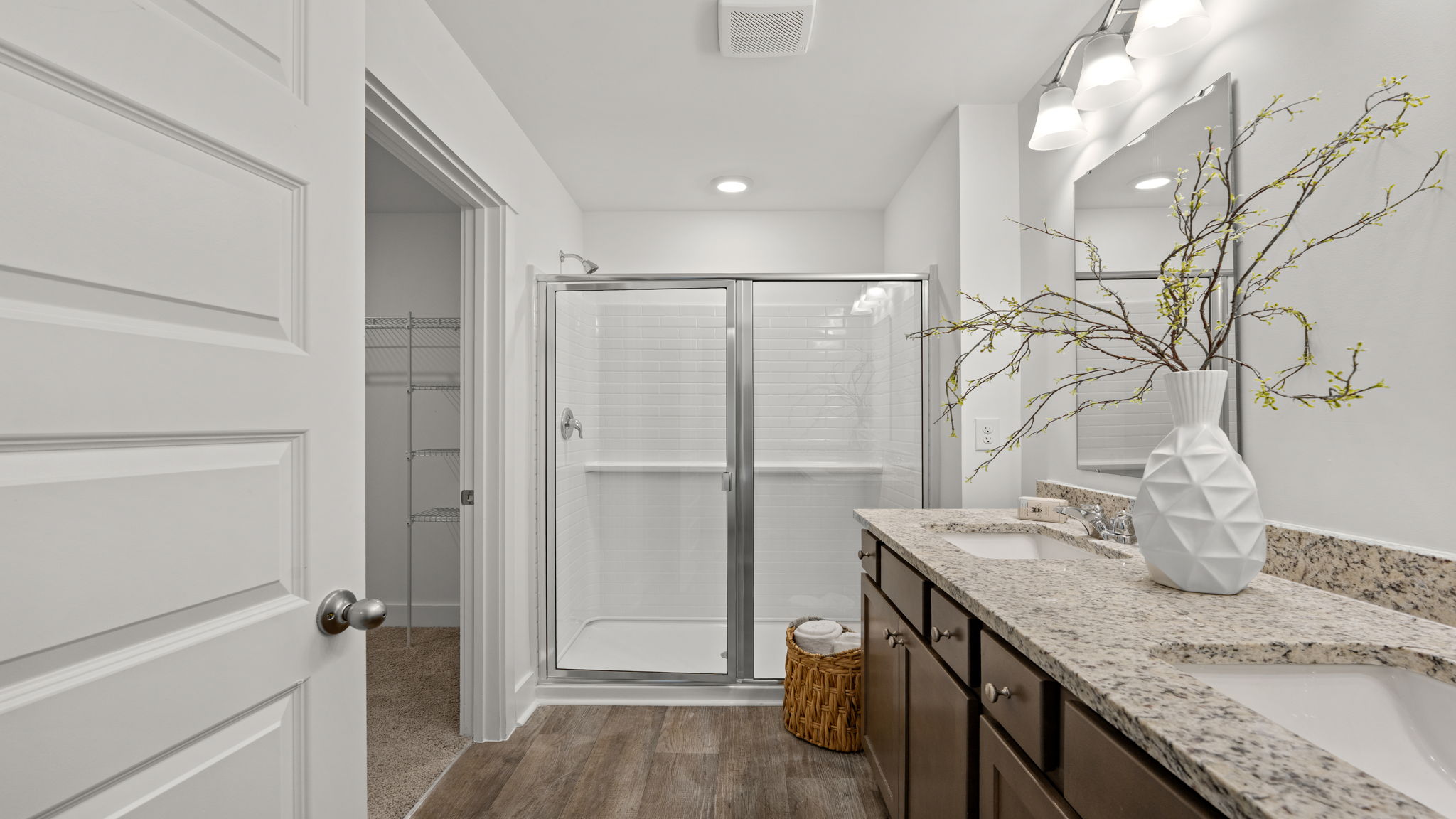 Bathroom with dual-sink vanity, dark cabinetry, large mirror, and glass-enclosed shower.