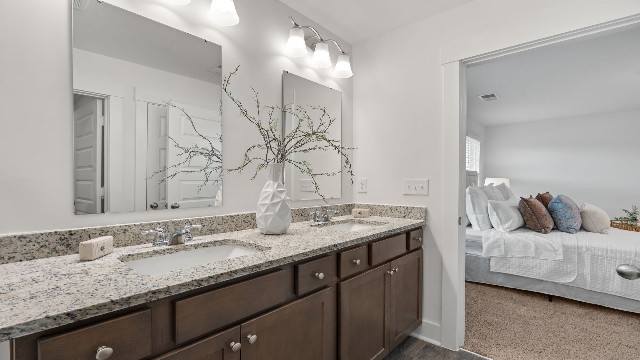 Bathroom vanity with dual sinks, dark cabinetry, large mirror, and granite-look countertop.