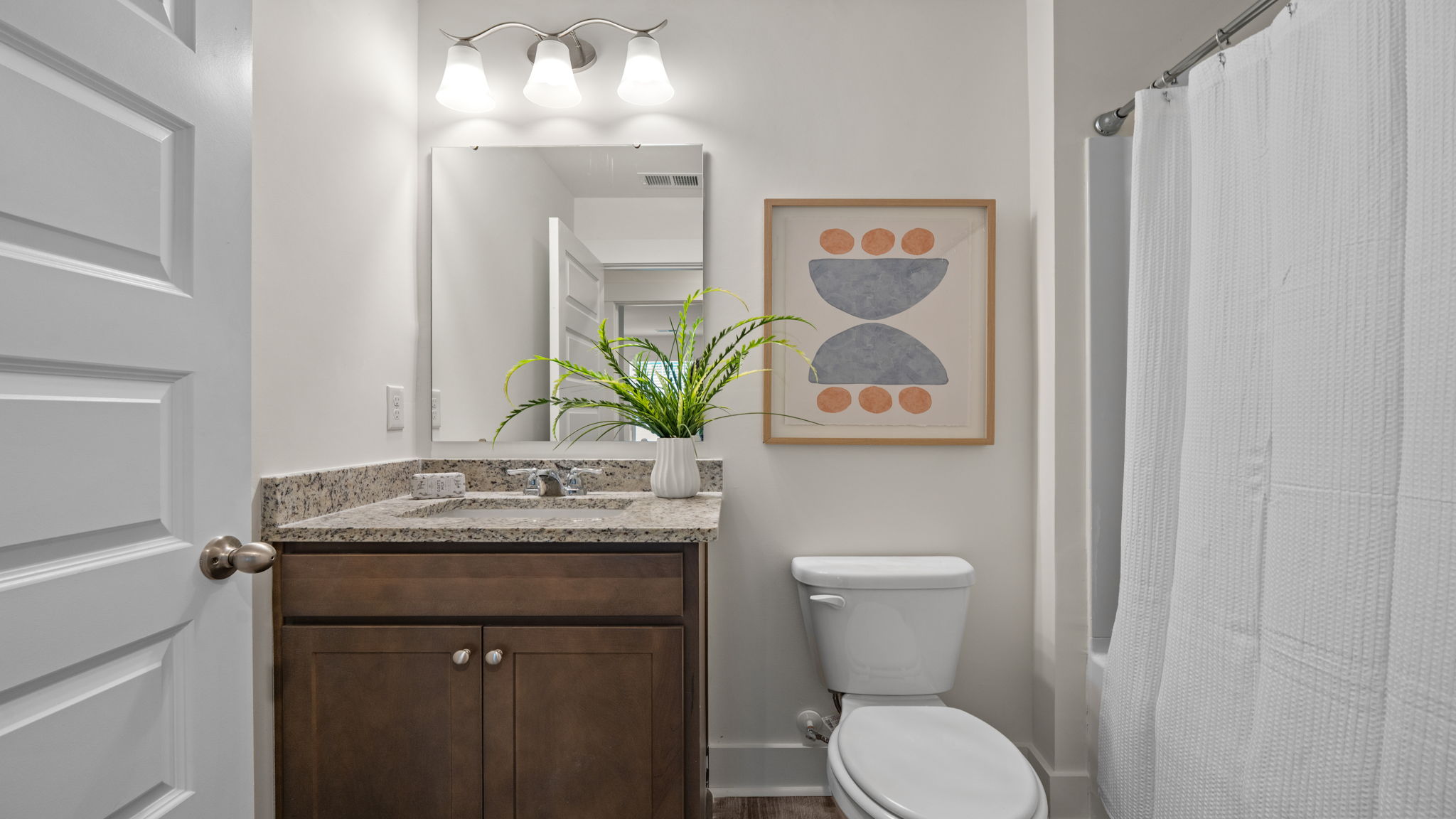 Bathroom with dark vanity, stone-look countertop, mirror, and white fixtures.