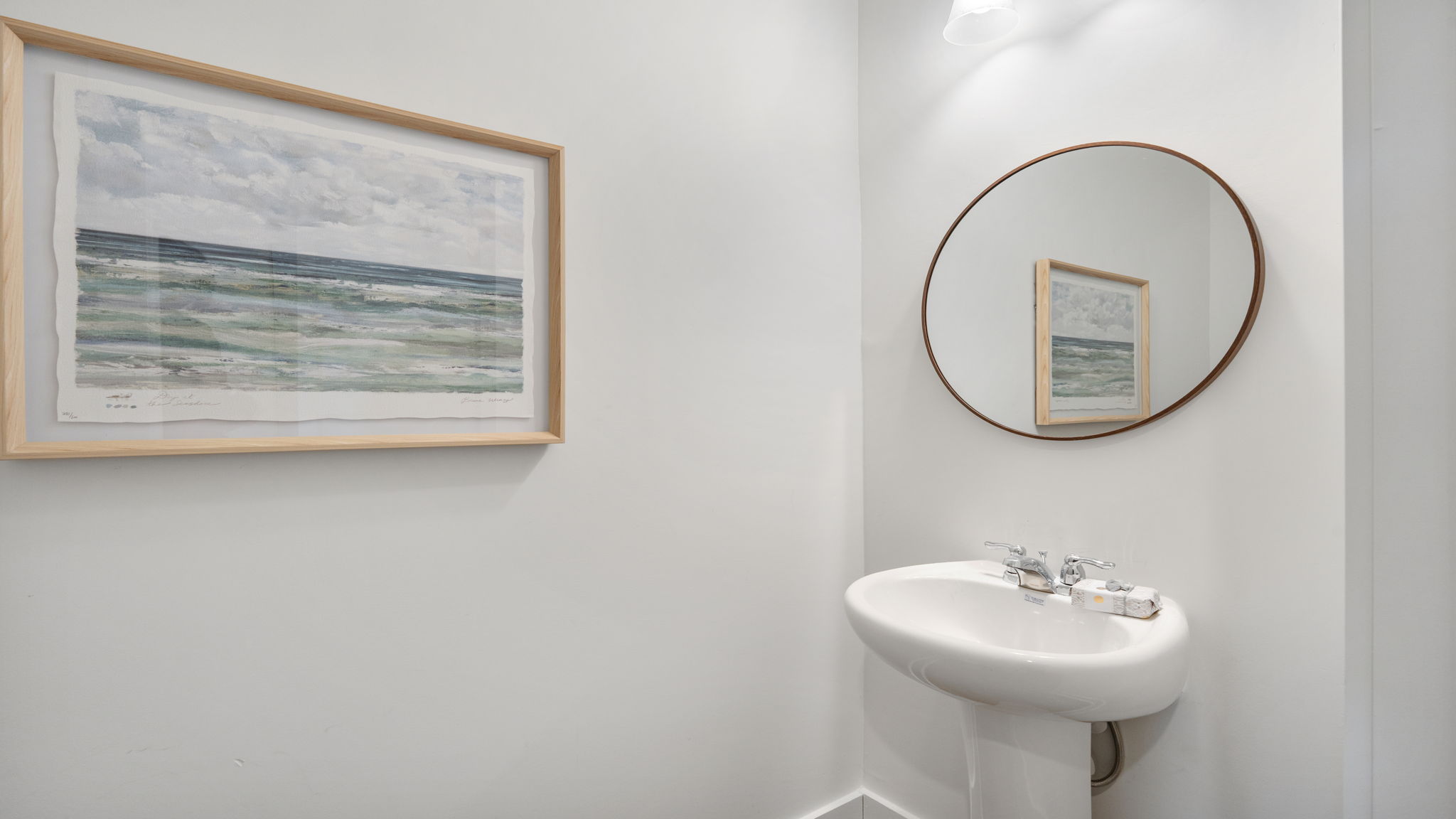 Powder room with pedestal sink, round mirror, and light neutral finishes.