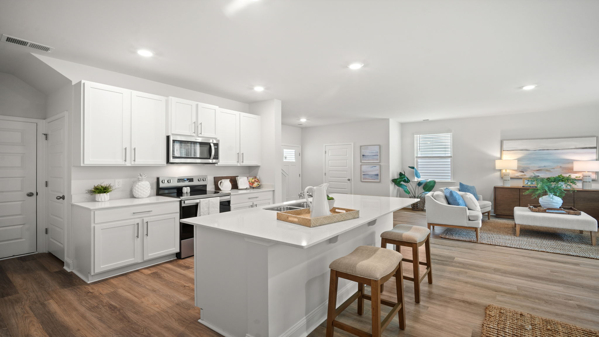 A spacious open floor plan living room and kitchen area with hardwood floors, and trey ceilings.