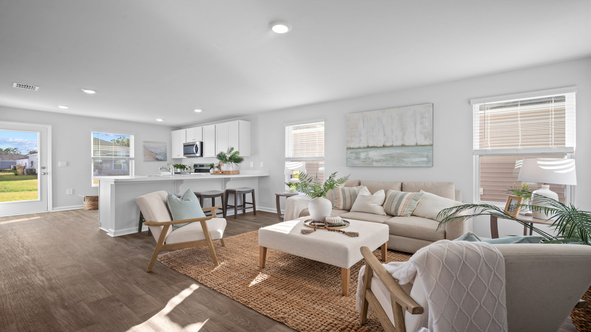 Open-concept living room in the Lewis floor plan at Rice Hope by D.R. Horton showcasing abundant natural light, spacious gathering areas, luxury flooring, and seamless connectivity to the kitchen and dining spaces.