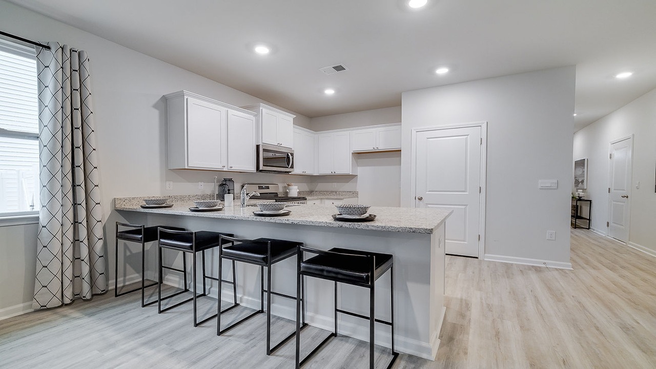 Bright chef-inspired kitchen in the Helena floor plan in Rice Hope showcasing abundant cabinet storage, spacious countertops, island seating, designer finishes, and seamless flow into the dining and living areas.