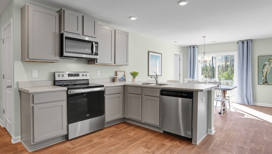 "Modern kitchen in the Macon floor plan by D.R. Horton featuring granite countertops, stainless steel appliances, designer cabinetry, and a spacious center island."