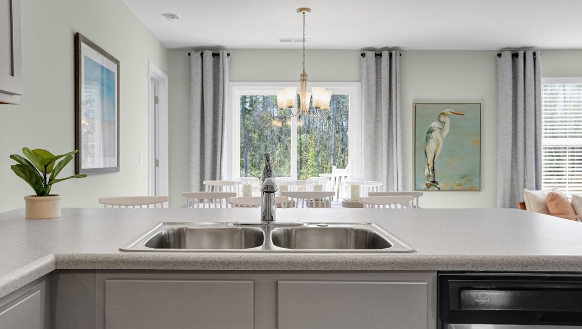 Modern kitchen in the Macon floor plan by D.R. Horton featuring granite countertops, stainless steel appliances, white cabinetry, and an oversized center island.