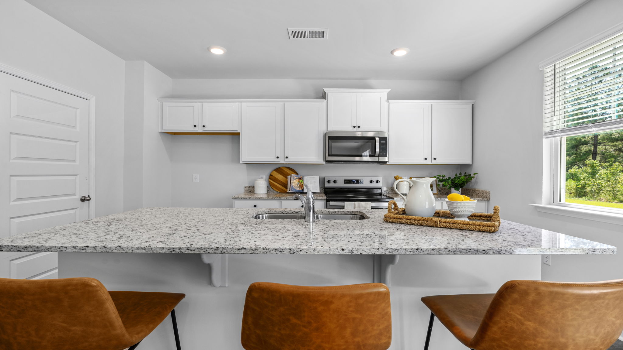 Spacious kitchen in the Belhaven floorplan showcasing a large island, sleek cabinetry, energy-efficient appliances, granite countertops, and seamless connectivity to the dining and living areas.