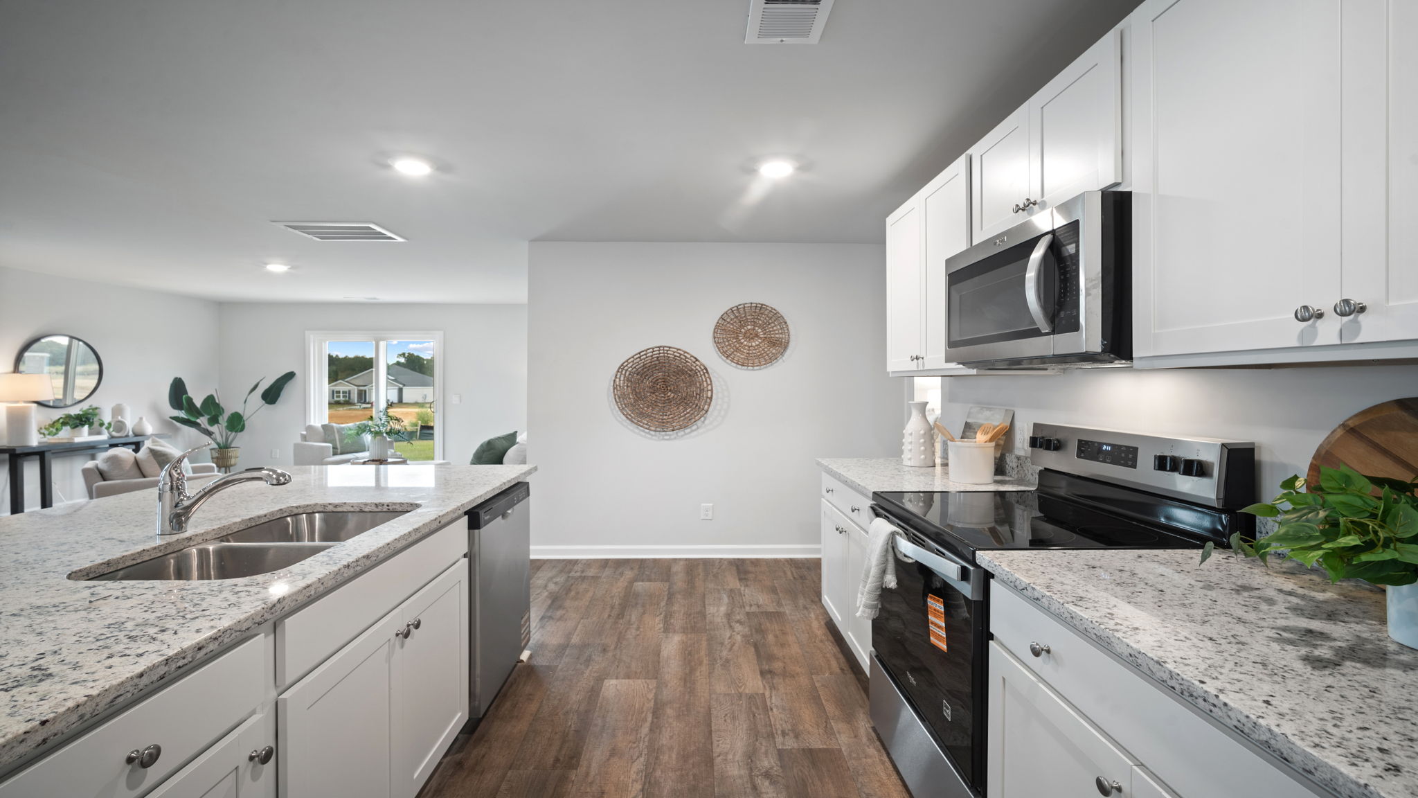 Side view of the kitchen area with granite countertops, large island, cabinets, tile backsplash, and stainless steel appliances with pantry in the corner.