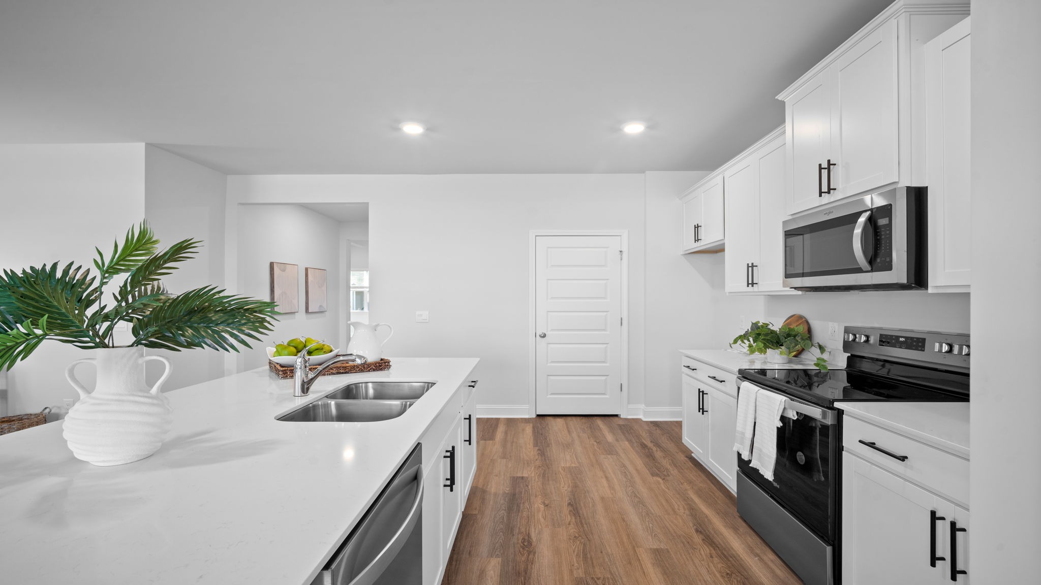 Side view of the kitchen area with granite countertops, large island, cabinets, tile backsplash, and stainless steel appliances with pantry in the corner.