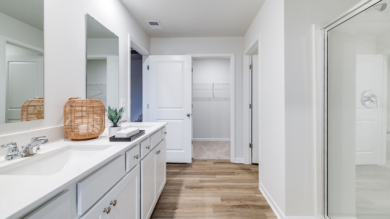 Primary bathroom in Hayden model featuring dual vanities and modern finishes with walk-in closet access.