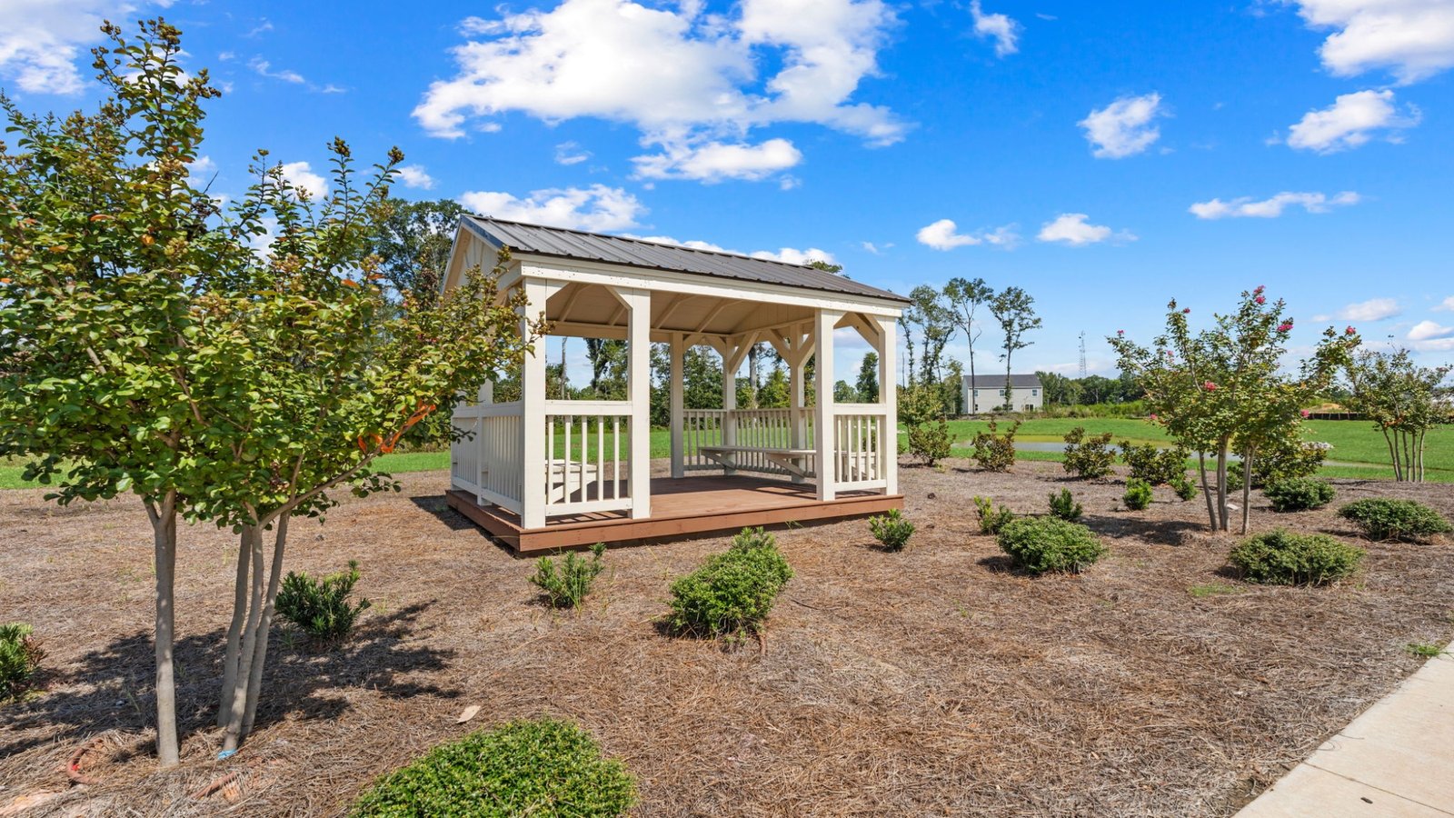 White community gazebo with covered seating area overlooking landscaped common space and walking areas.