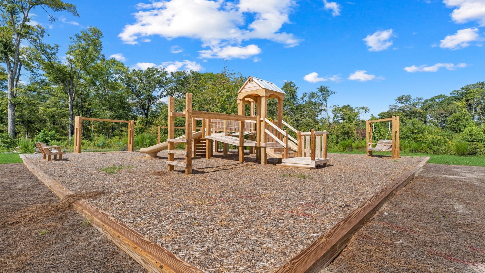 Wooden playground with slides, climbing features, swings, and seating in a community recreation area.
