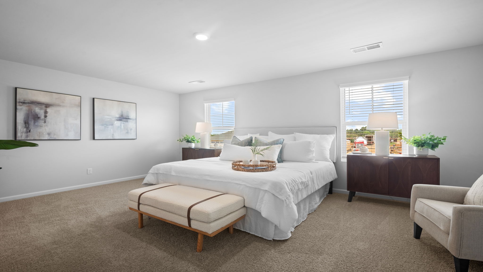 Primary bedroom decorated  with a bed, bench, side table and chair