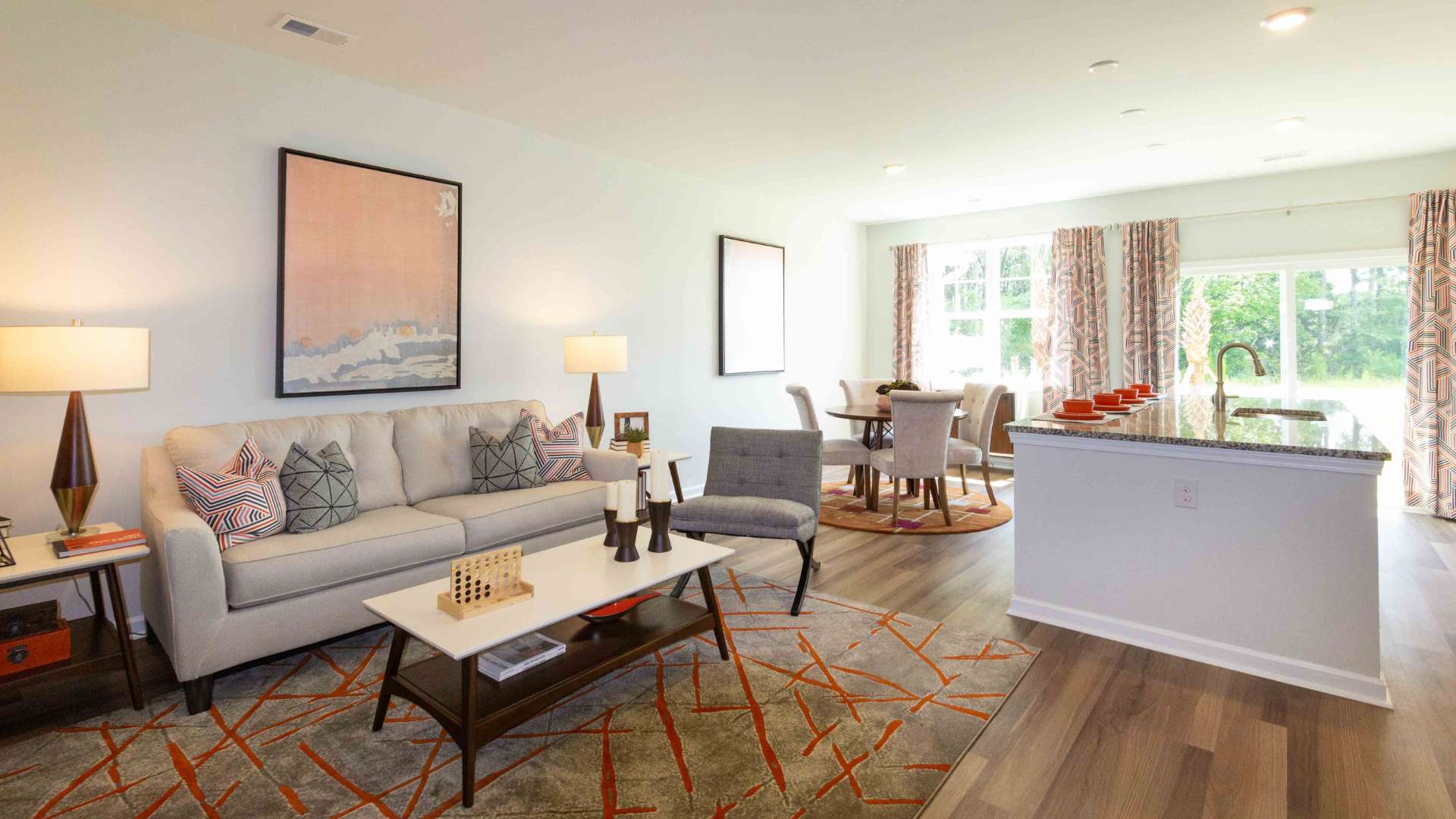 Open-concept living room with sofa seating, accent chairs, area rug, artwork, and large rear windows.